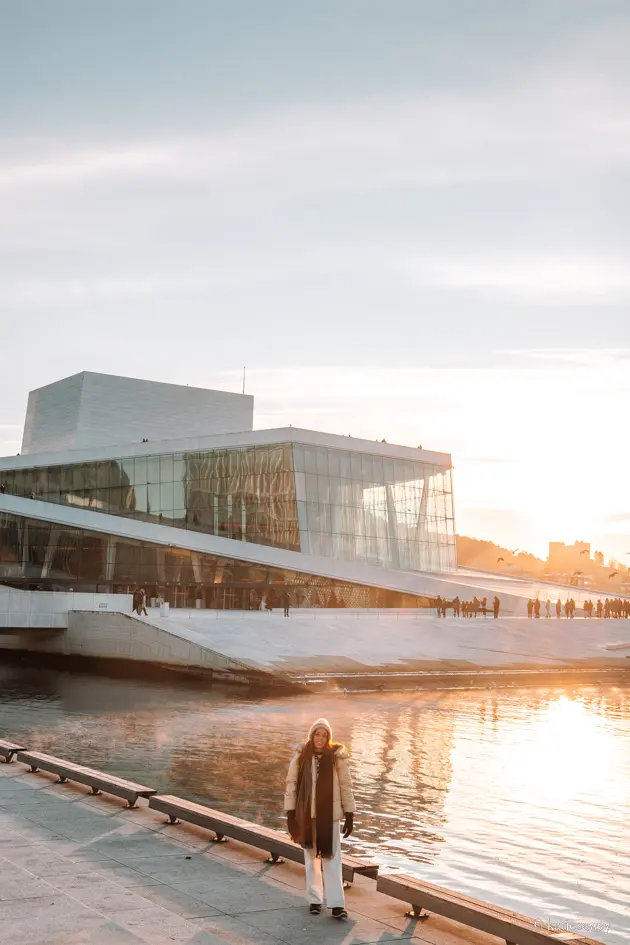 girl standing outside the oslo opera house in winter sunlight with an orange reflection on the water