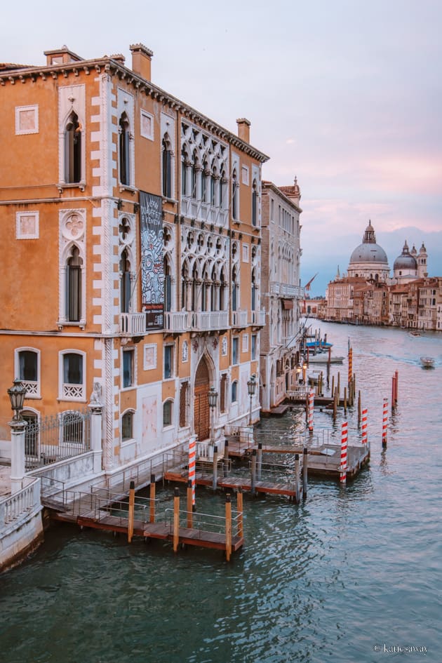 the harbour of venice canal with little docks and stripy red poles and the basilica in the background