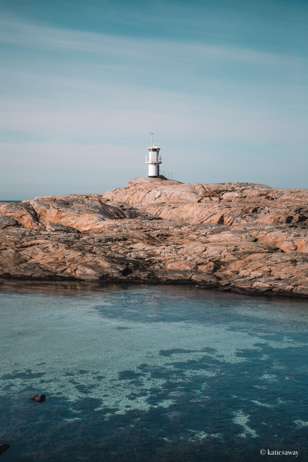 Skallens lighthouse on marstrand - a white lighthouse on a cliff with translucent blue water infront