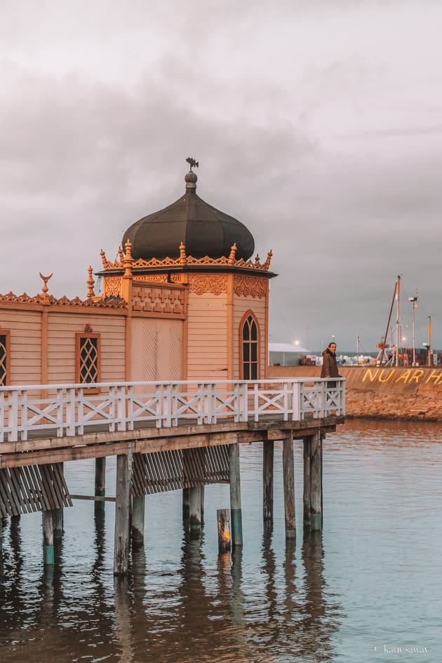 varberg kallbadshus in the sunset. there is a white terrace and the building is yellow, wooden with a black dome on the roof