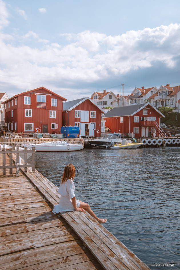 girl sat on the harbour in klädesholmen with red boat houses behind