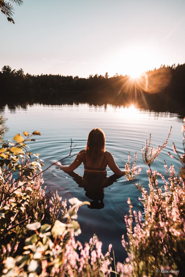 girl swimming in a lake at sunset surrounded by pink flowers