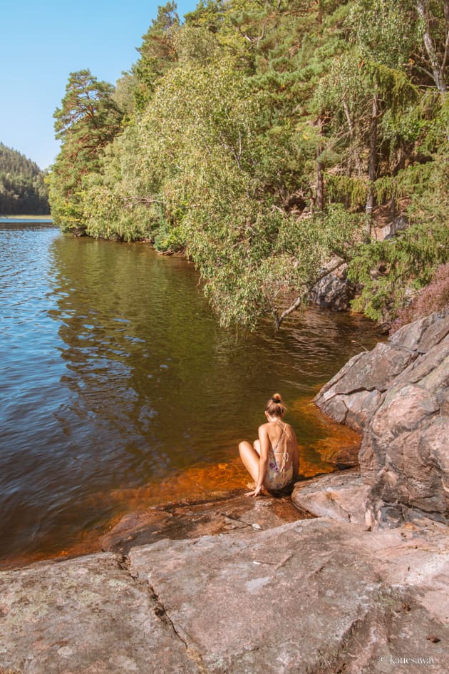 girl in a yellow swimsuit sat on a rock looking down at lake water in nääs