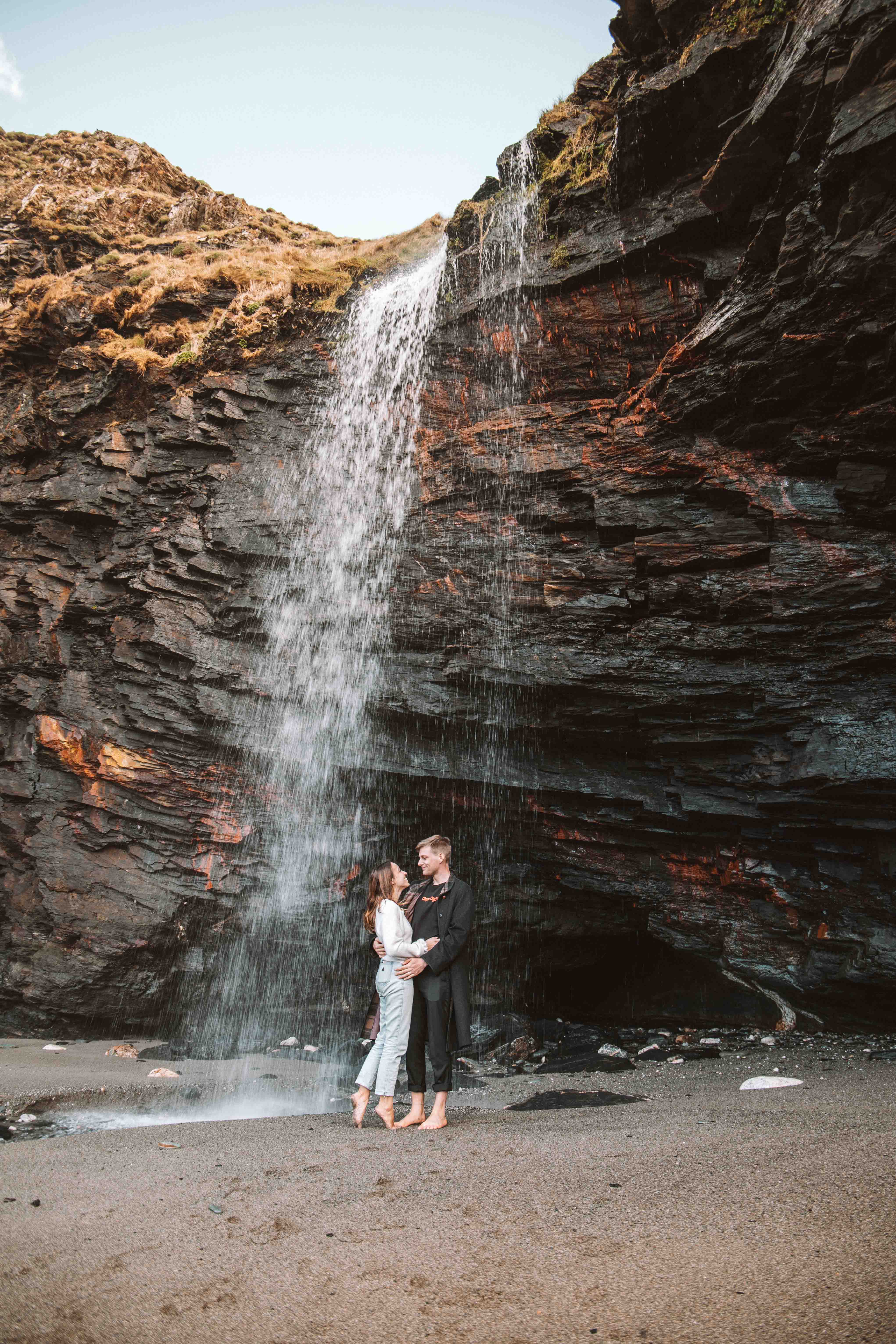 couple standing under a waterfall at the beach on a road trip