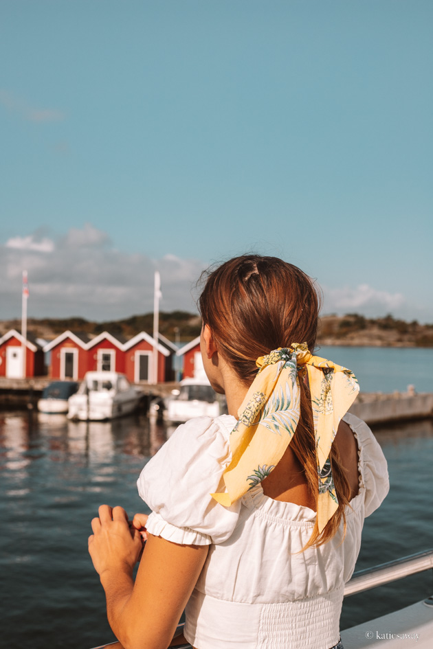 girl with a white shirt and yellow hair tie looking out over a row of red boat houses in the gothenburg archipelago
