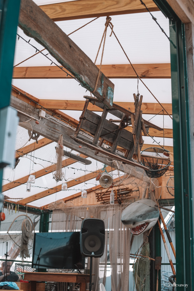 The ceiling of the outdoor seating area at Fiskeboa Vrångö with fishing nets, a wooden shark, a wheelbarrow and lights hanging down