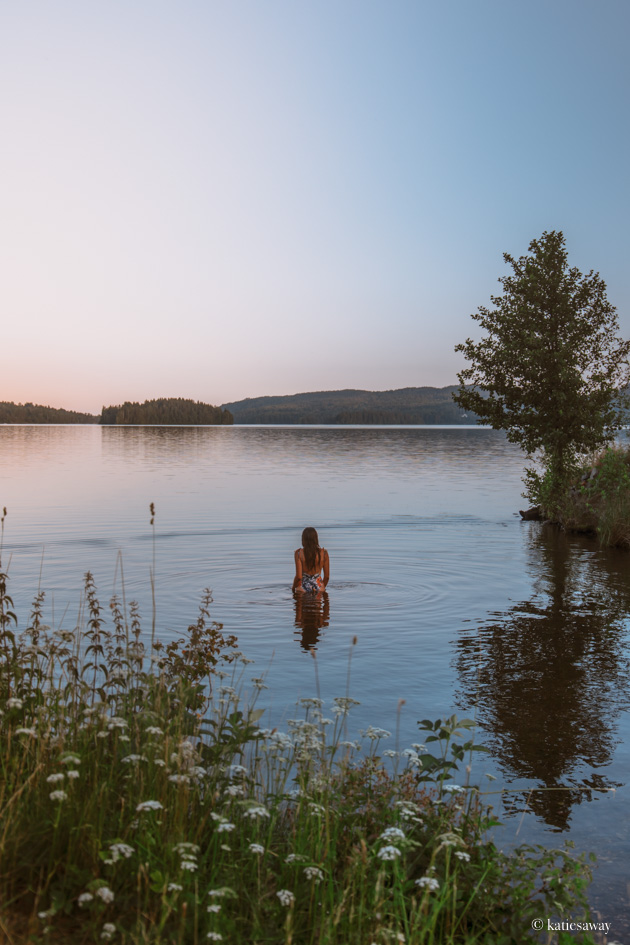 A girl wild swimming in a lake at sunset
