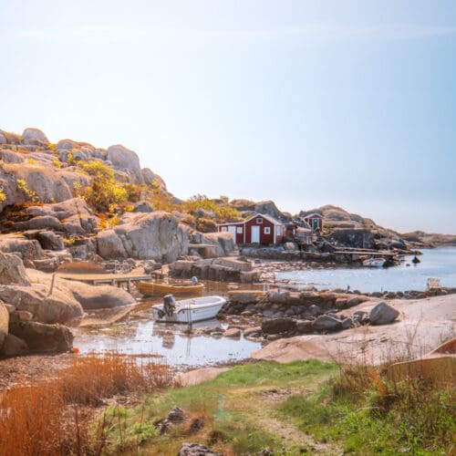A small harbour with ocks and a grass walkway. In the harbour is a small white moto boat and a red wooden boat house