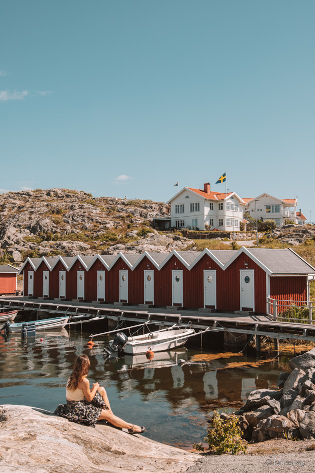 A girl sat on a rock infront of a row of red boat houses on teh island of styrsö