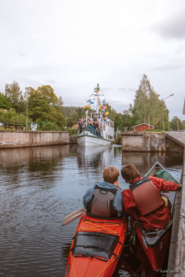 Two men in kayaks parked by the dock looking out into the Dalsland canal as the canal boat passes by